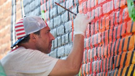 Artist painting a colorful mural on a brick wall.