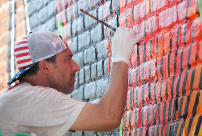Artist painting a colorful mural on a brick wall.