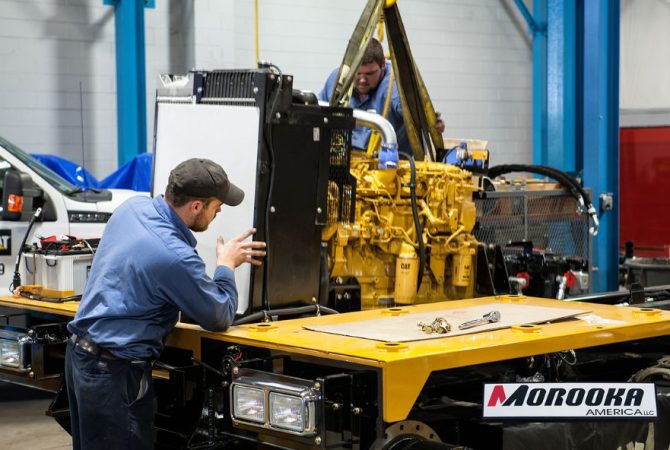 Two workers assemble heavy machinery at Morooka America’s U.S. manufacturing facility.